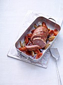 Meatloaf wrapped in bacon with tomatoes and onions in a roasting tin