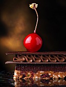 A layered chocolate dessert topped with a candied cherry (close up)