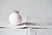 A white egg with a feather on a newspaper