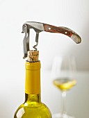 A bottle of white wine being open with a sommelier knife