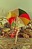 A woman on a beach holding a large parasol and cool bag