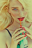 A blonde woman with red lipstick and fingernails drinking from a can with a straw