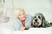 A blonde woman and a dog lying on a bed