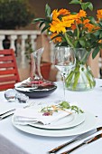 Weiß gedeckter Tisch mit Rotweinkaraffe und orangefarbenem Blumenstrauss