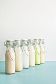 Various types of milk substitutes in bottles with their ingredients: almond milk, rice milk, coconut milk, oat milk, Edamame milk, soya milk