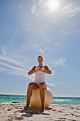 Frau macht Yogaübung auf Gymnastikball sitzend am Strand