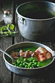 Cream of pea soup with fried bacon on a wooden table