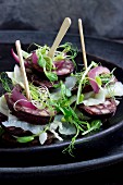 Pumpernickel-Millefeuille mit Rotwurst, Weißkraut, Sprossen auf schwarzen Tellern