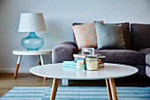 Round retro coffee table in front of sofa with scatter cushions and table lamp on side table