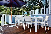 White outdoor chairs and table on terrace with blue parasol and white wooden balustrade