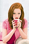 A red-haired woman wearing pink clothing holding a coffee mug