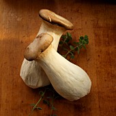 Two king trumpet mushrooms on a chopping board with a sprig of fresh marjoram