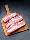 Three slices of pork belly on a chopping board