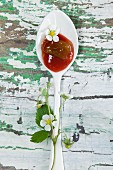 Strawberry and rhubarb jam on a spoon with strawberry leaves on a wooden table