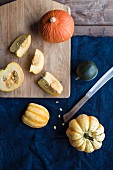 Various pumpkins, partially sliced, on a chopping board and a blue cloth