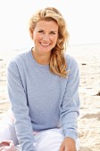 A blonde woman on a beach wearing a blue jumper