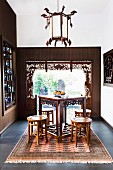 Carved counter table with stool on carpet in front of window with carved wooden element