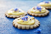 Shortbread biscuits topped with lemon curd and cornflowers on a blue surface
