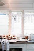 Paper garland and fairy lights in front of kitchen window and pine cones in decorative glass as Christmas decorations