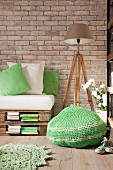 Green crocheted pouffe, pallet sofa and standard lamp on wooden tripod in vintage interior