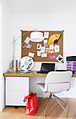 Pin board above desk with white upholstered chair