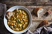 Tuscan bean soup on a wooden surface with wholemeal bread