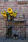 Sunflowers in vintage tin on metal welly stand against brick wall