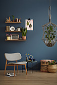 A shelf on a blue wall, a grey chair, a side table, basket and a hanging basket in a living room