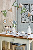 Table set with small cakes and coffee outside wooden shed decorated with bunting