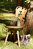 Wooden chair, hiking utensils, wine bottle wrapped in map and walking boots below tree