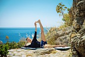 A woman exercising on rocks above the sea