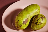 Two ripe pawpaws on a pink plate