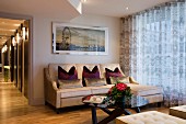 Elegant seating area with sofa and round coffee table next to glass wall with floor-length curtains