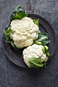 Two fresh cauliflowers on a metal plate (seen from above)