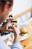 A man taking a photo of a burger with a smart phone