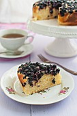 A slice of blueberry cake with icing sugar served with a cup of tea
