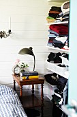 Lamp on antique side table next to open-fronted shelves of clothes on white wooden wall