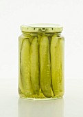 Sliced gherkins in a screw-top jar on a white surface