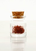 Saffron threads in a glass bottle with a cork on a white surface
