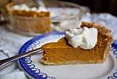 A slice of pumpkin pie with a dollop of cream on the blue and white plate