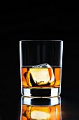 Ein Glas Whiskey mit Eiswürfel vor schwarzem Hintergrund