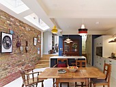 Open-plan kitchen with traditional dining area, antique glass-fronted cupboard against blue partition, strip of modern skylights with white frames and brick wall