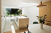Vase of flowers on dining table in open-plan, white, designer kitchen with skylight and glass wall with view into summery garden