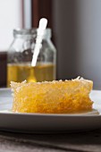 A honeycomb on a plate with a jar of honey in the background
