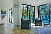 Living area with two dark, wicker armchairs in front of French windows with view of trees in garden