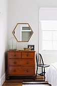 Vintage chest of drawers in front of polygonal mirror in corner of bedroom