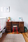 Wooden stool with red lacquered frame in front of solid wood desk next to cot