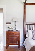 Wooden bedside table with table lamp next to bed with canopy frame