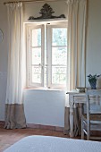 Floor-length curtains on open lattice window and vintage desk and chair in bedroom