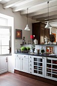 Kitchen counter with white, country-house-style base units and raised bar below pendant lamps